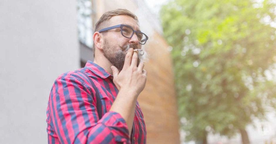 un hombre de camisa a cuadros fuma un puro de marihuana a las afueras de un edificio