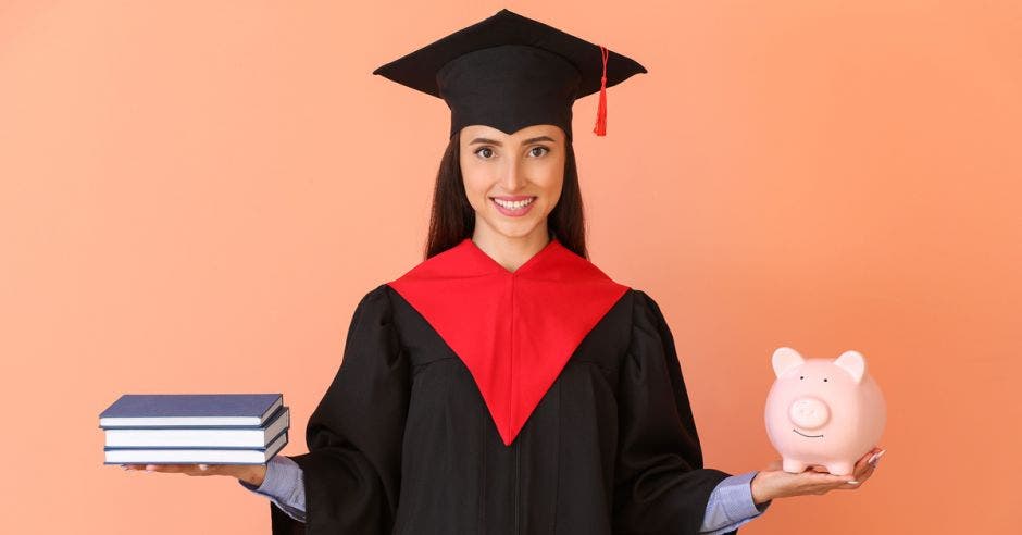 joven estudiante con toga y birrete, sosteniendo libros y alcancía de cerdito